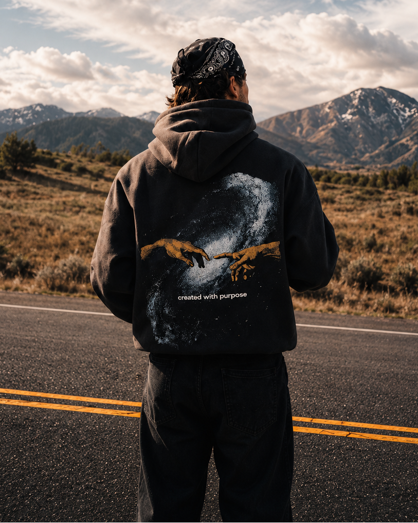 Person standing on a road looking at mountains with a scenic view wearing a christian hoodie that says created with purpose