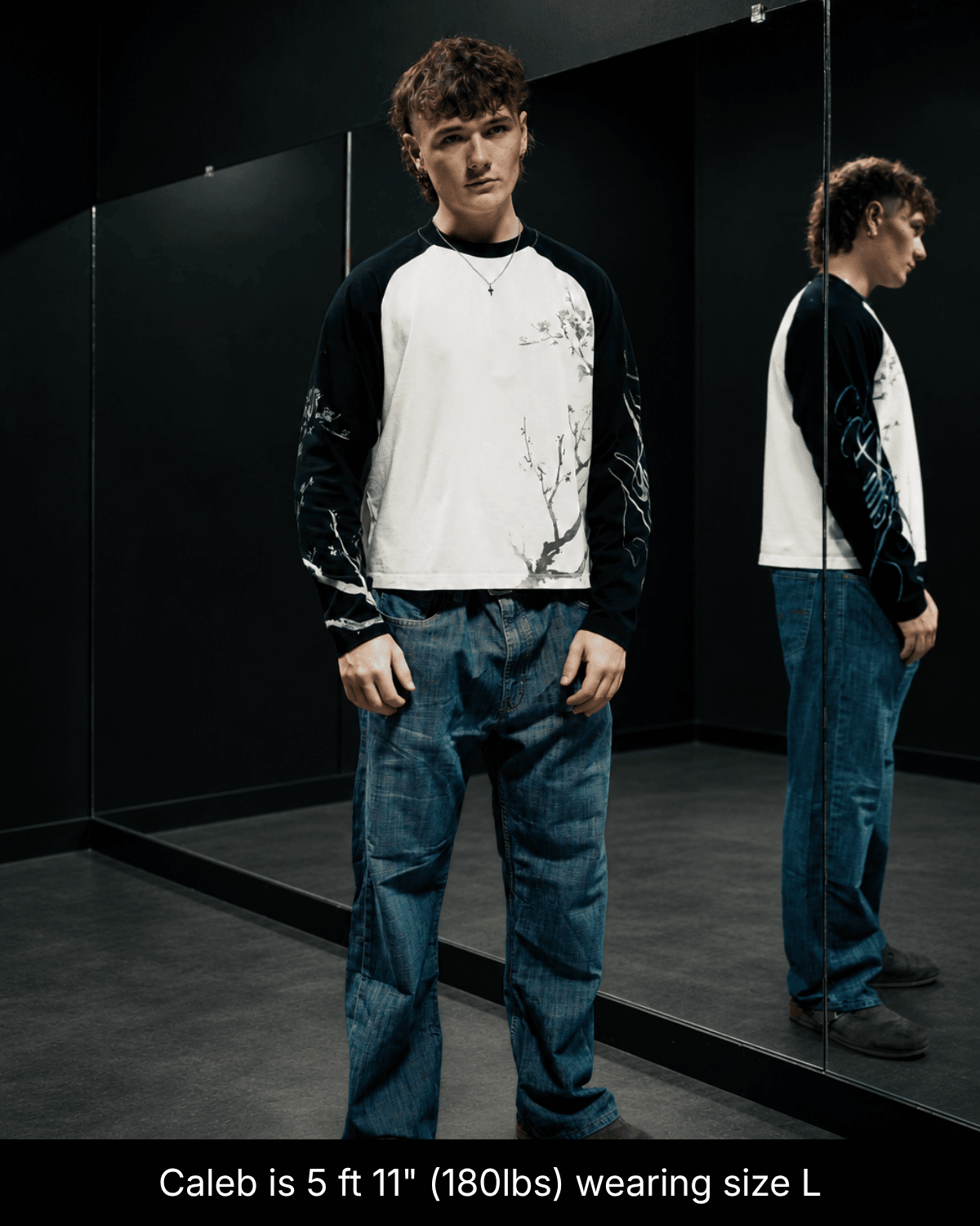 Full-length view of a model wearing the black and white John 15:5 long sleeve shirt in size L beside a mirror.