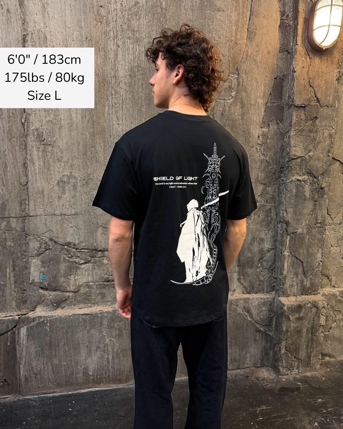 Shield Of Light faith based t-shirt black back graphic worn by model outdoor wall